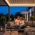Ein Paar sitzt abends auf einem Lounge-Sofa unter einer beleuchteten Pergola.