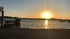 Sonnenuntergang über dem Meer mit Booten und einem Steg im Vordergrund daneben liegt die Bikini Bar.
