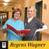 Zwei lächelnde Frauen in Krankenpflegeruniformen, eine hält einen roten Ordner. „Regens Wagner“ Logo.