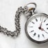 Antike silberne Taschenuhr mit Kette und römischen Ziffern auf hellem Hintergrund.