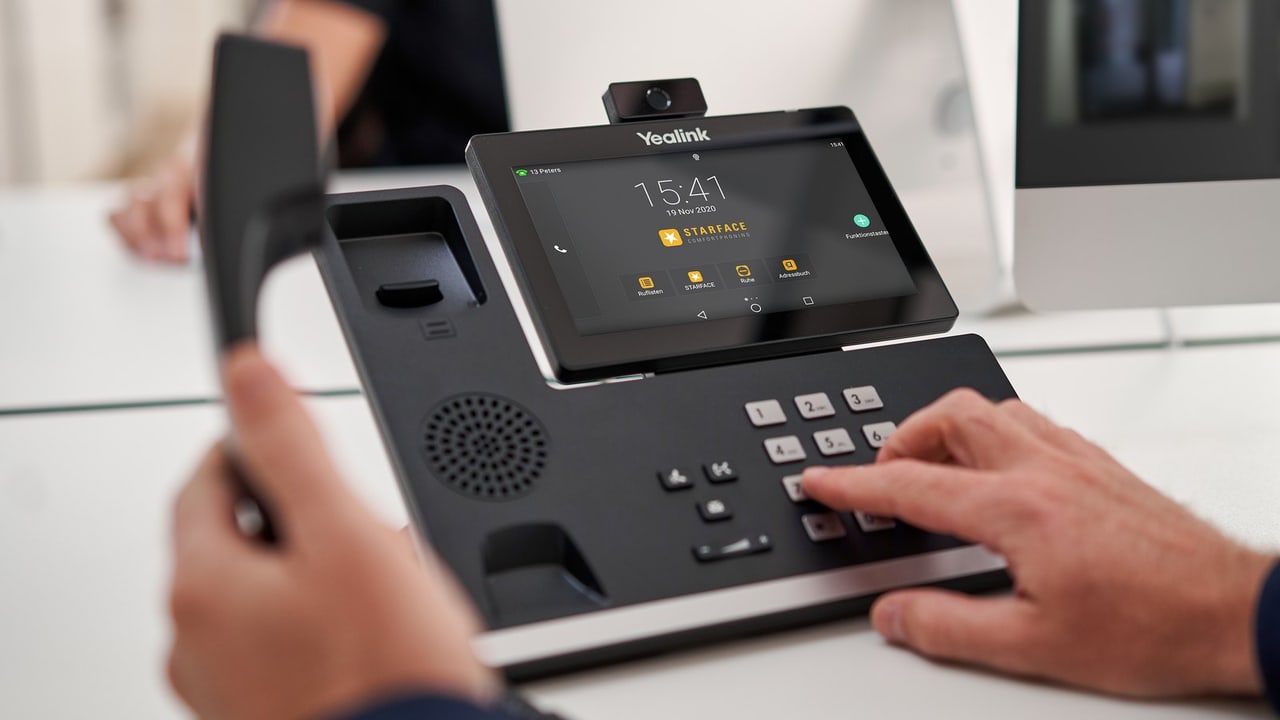 Yealink-Tischtelefon mit Farbdisplay und STARFACE-Oberfläche, eine Hand wählt