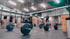 Mehrere Langhanteln mit Gewichtsscheiben liegen auf dem Boden einer CrossFit-Box mit Turnringen und Holzboxen im Hintergrund.