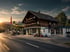 Chalet-Gebäude mit Agrola Tankstelle, Schweizer Flagge und Ladengeschäft an einer Landstraße bei Sonnenuntergang.