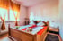 Schlafzimmer mit orangefarbenen Vorhängen, einem Doppelbett aus hellem Holz und zwei orangefarbenen Laken.