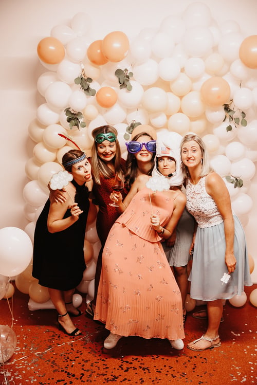 Feiernde Frauen mit Partyrequisiten vor einer Ballonwand