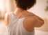 A short-haired person in a grey tank top seeks neck pain relief.
