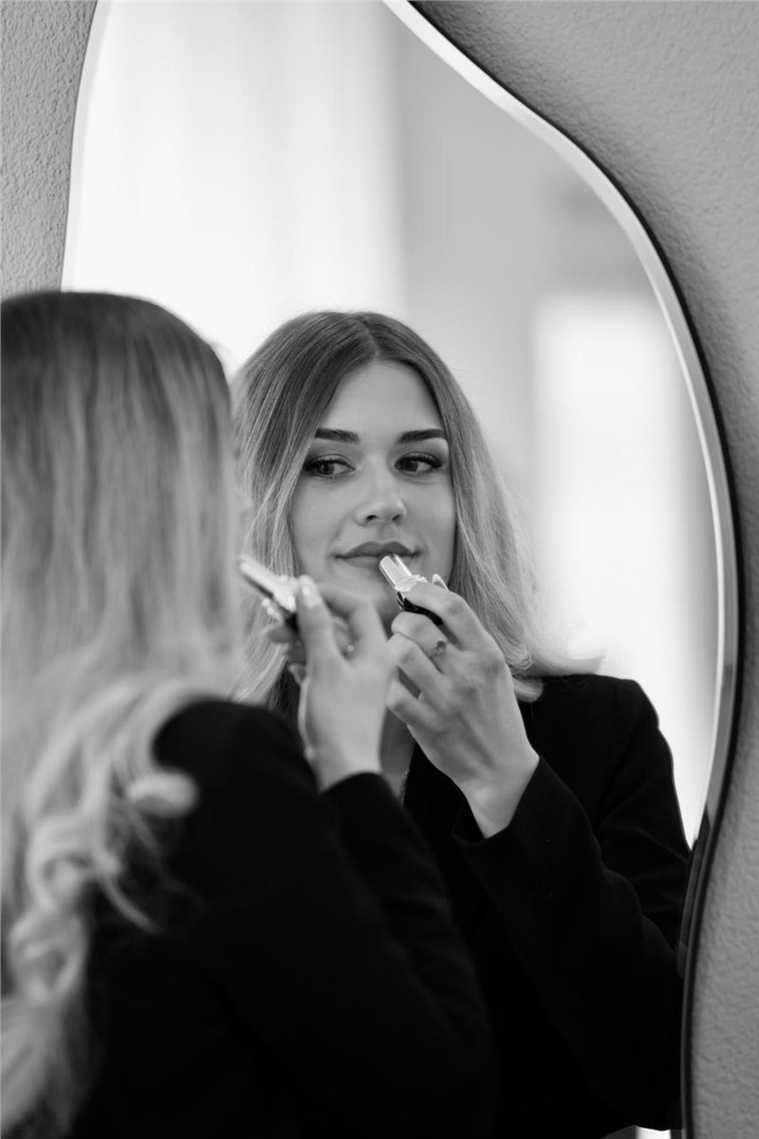Maria trägt in einer Schwarz-Weiß-Aufnahme Lippenstift vor einem geschwungenen Spiegel auf.