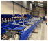 Lange blaue Förderbandstruktur mit Rollen und Metallrahmen in einer Werkshalle.