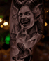 Schwarz-graues Tattoo einer lachenden Frau mit Hörnern, spitzen Ohren, einem Kirchturm und einer Kapuzenfigur.