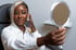 A woman is holding a hand mirror, looking at her reflection after receiving anti-aging skin treatments.