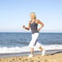 Elder woman jogging on a sandy beach with her new custom orthotics.