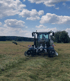 Ein Traktor mit einem Mähwerk mäht ein Feld unter blauem Himmel mit Wolken.