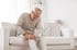 A senior man with knee pain sitting on a sofa.