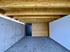 Ein überdachter Außenbereich mit Holzbalkendecke, Betonwand links, weißer Wand rechts, schwarzer Tür und Holzverkleidung.