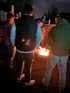 Mehrere Menschen stehen im Dunkeln um ein hell loderndes Lagerfeuer.