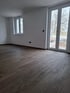 Leerer Raum mit dunkelbraunem Holzboden, weißen Wänden und zwei Fenstern.
