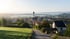 Bayerisches Dorf mit Zwiebelturmkirche im morgendlichen Nebel, umgeben von grünen Wiesen und Hügeln bei Sonnenaufgang in Garching an der Alz