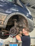 Ein Mechaniker arbeitet an der Radaufhängung und Bremse eines aufgebockten, schmutzigen blauen Vans.