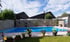 Ein blauer Pool mit Gabionenwänden und Topfpflanzen unter blauem Himmel mit weißen Wolken.