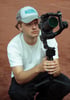 Ole von Küstencontent mit Basecap und weißem T-Shirt, der eine Kamera mit Gimbal auf einem roten Sandplatz bedient, mit fokussiertem Blick.