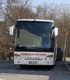 Weißer Reisebus mit "HÜBNER-REISEN" und "SETRA" Schriftzug, geparkt vor Bäumen.