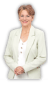 Eine lächelnde Frau mit kurzem braunem Haar, einer hellgrünen Jacke und weißem Oberteil hält ihre Hände vor sich.