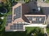 Dach eines Einfamilienhauses mit zahlreichen schwarzen Solarmodulen und grünem Rasen.