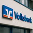 Blaues und oranges Volksbank-Logo mit Schriftzug an einer hellen Gebäudefassade.