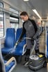 Reinigungskraft säubert einen blauen Zugsitz mit einem Kärcher Waschsauger in einem Zugabteil.