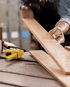 Eine Person hält ein Holzbrett über einem Holztisch mit einem gelben Maßband.