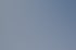 Graue Drohne mit orangefarbenen Propellerarmen schwebt über einer orangefarbenen Flagge und einem Gebäude.