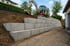 Mehrstufige Betonmauer mit Bagger, der Erde auf der Baustelle neben einem Haus bewegt.