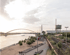 Weite Ansicht eines Flusses mit einer orangefarbenen Bogenbrücke, einem Sandstrand und Bahngleisen am Ufer.