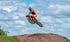 Ein Motocross-Fahrer in orangefarbener Ausrüstung springt auf einem orangefarbenen Motorrad über einen Erdhügel.
