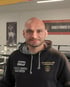 Kahlköpfiger Mann mit Bart im schwarzen Kapuzenpullover "FIGHTCLUB LANGENAU" und "TP60" vor Boxring.