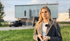 Eine junge Frau steht vor einem Containerhaus und einem Auto auf einer grünen Wiese.
