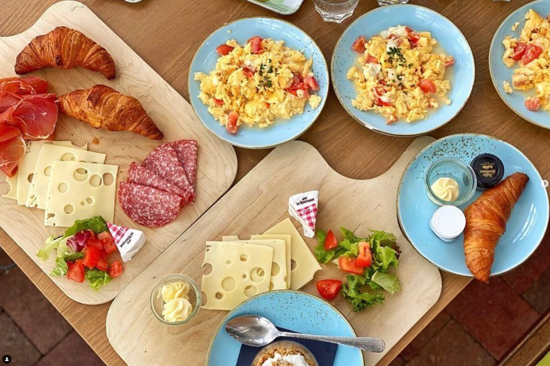 Gedeckter Frühstückstisch mit Rührei, Croissants, Käse und Schinken