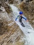 Ein Canyoning-Teilnehmer in Neoprenanzug und blauem Helm rutscht einen Wasserfall hinunter.