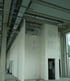 Ein unfertiger Innenraum mit weißen Wänden, Betonsäulen und sichtbaren Lüftungsrohren an der Decke.