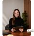 Lachende Frau mit Brille und schwarzem Rollkragenpullover hält ein Tablet an einem Holztisch, daneben Laptop.