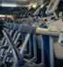 Eine Reihe von modernen Crosstrainern steht nebeneinander in einem Fitnessstudio für das Ausdauertraining bereit.