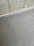 Grauer gesprenkelter Boden mit einer Fuge und einer weißen Fußleiste an einer grauen Wand.