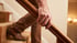 A person's hand grips a wooden handrail while walking up carpeted stairs in a home.