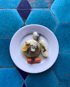 Artichoke heart with lemon, potatoes, carrots, and dill on a white plate, on a blue tiled table.