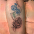 Tattoo auf einem Arm mit einer detaillierten Hundepfote, blauen Blumen und grünen Blattranken.