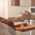A gloved hand holds a syringe filled with yellow liquid near a patient's shoulder, with a medicine vial on a tray nearby.