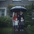 Familie vor dem Haus im Regen unter einem Regenschirm
