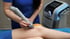 Therapist uses a grey shockwave therapy device on a patient's knee.