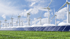 Windturbinen und Solarpaneele in einer Reihe auf grünem Gras unter blauem Himmel.