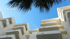 Weiße Hotels mit Balkonen unter blauem Himmel und Palmenblatt; Text: Hotels